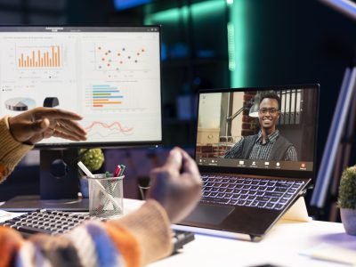 Young adult employee attends a meeting on video conference, presenting the current economic situation within the enterprise. African american guy having virtual communication with coworkers.